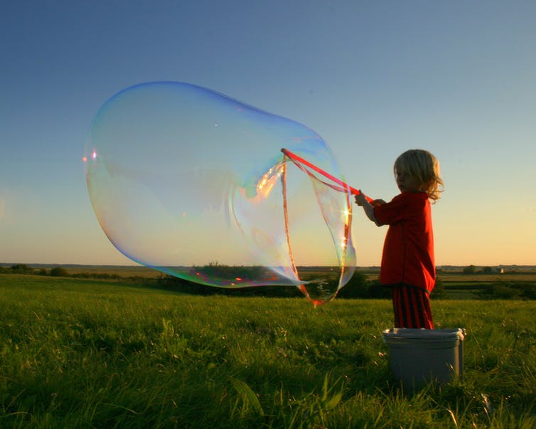 A boys makes a large soap bubble.